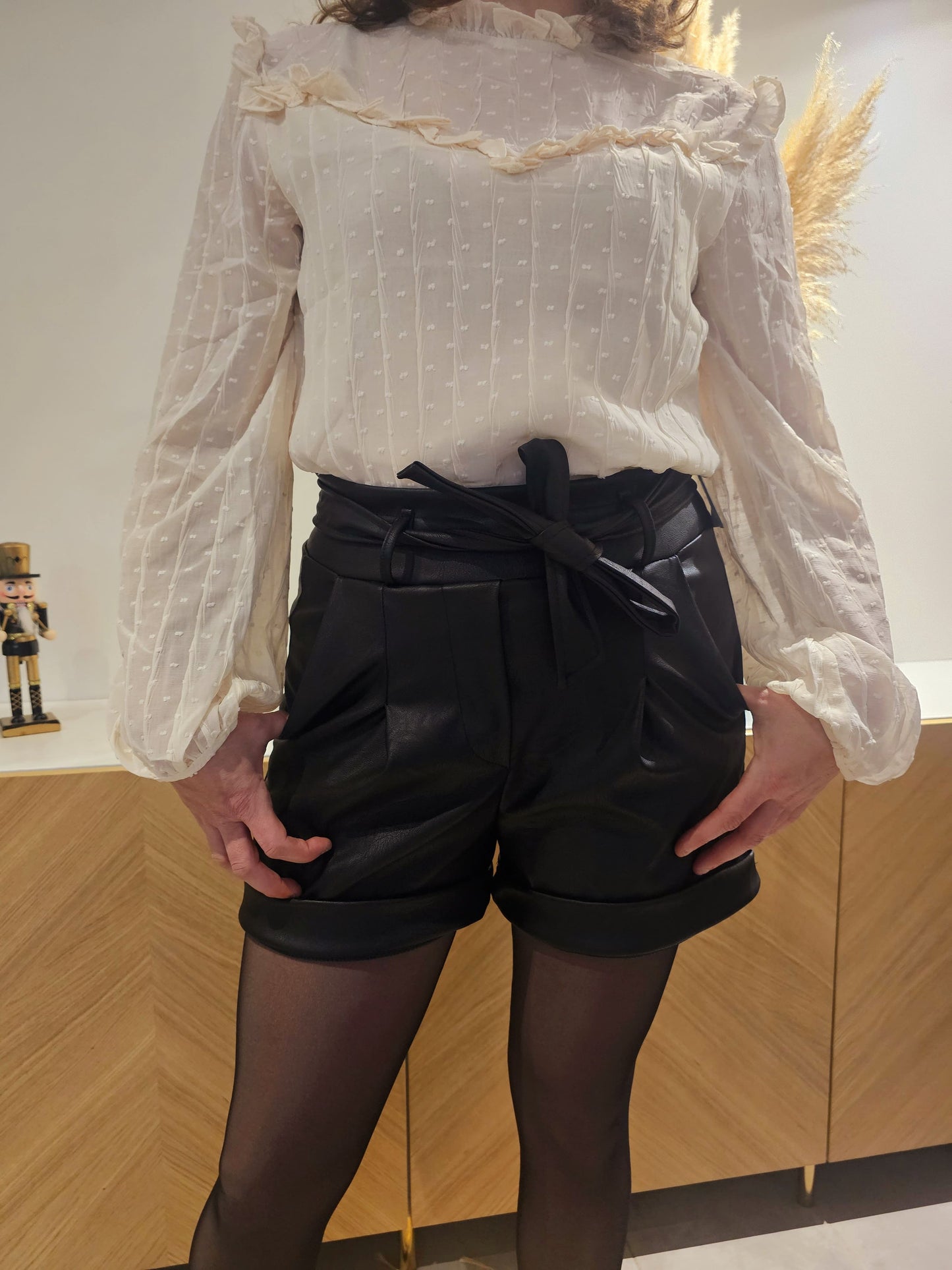 Short en similicuir noir avec deux poches latérales, des fronces sur le devant et une taille élastique. Ce short est muni d'un revers sur le bas et d'une ceinture amovible incluse pour un look tendance et polyvalent.