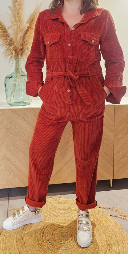 La combinaison Elina est en velours rouille de qualité, avec un col chemise élégant et des poches plaquées au niveau de la poitrine. Elle se ferme par des boutons sur le devant et dispose de poches latérales de style western. La ceinture assortie accentue la coupe droite de cette tenue. Taille du S au L