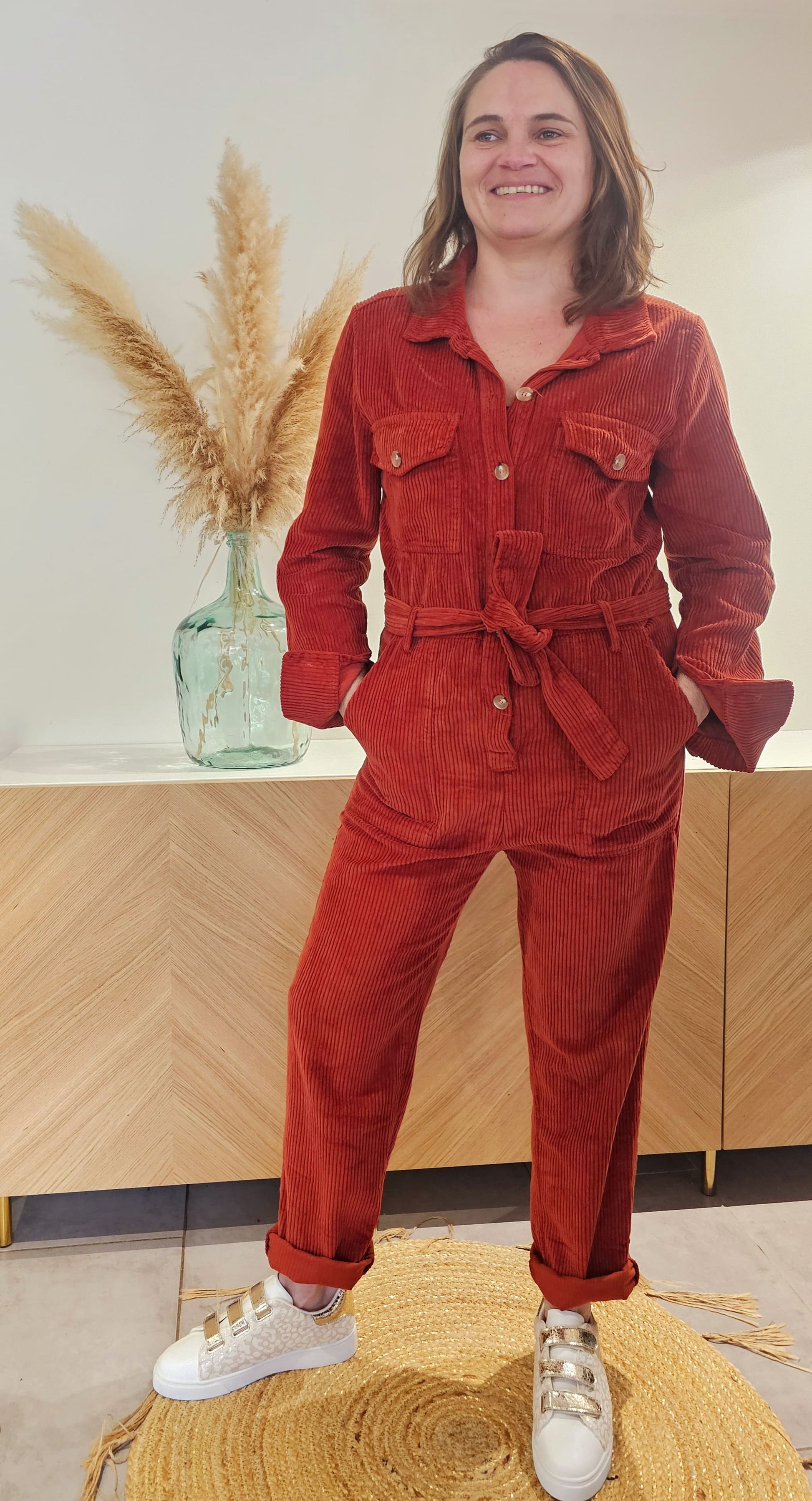 La combinaison Elina est en velours rouille de qualité, avec un col chemise élégant et des poches plaquées au niveau de la poitrine. Elle se ferme par des boutons sur le devant et dispose de poches latérales de style western. La ceinture assortie accentue la coupe droite de cette tenue. Taille du S au L